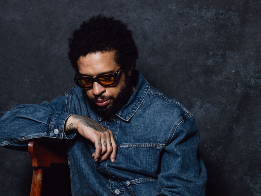 Kenneth Whalum in denim, seated sideways on a wooden chair, looking down